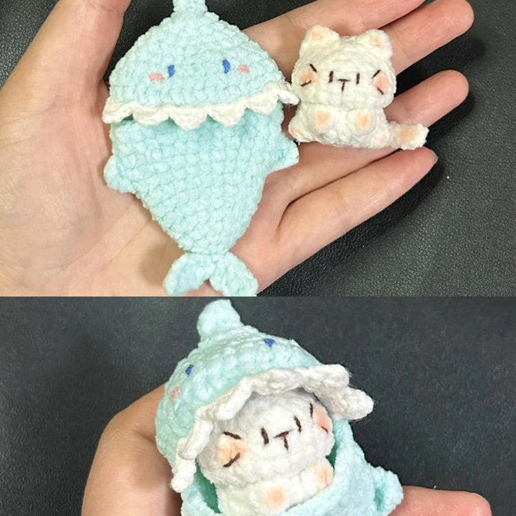 Two small crochet toys, one resembling a fish and the other a cat, held in a hand against a dark background.